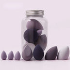 A set of multicolored spherical beauty egg makeup sponges in gray and purple made of hydrophilic polyurethane surrounding a jar