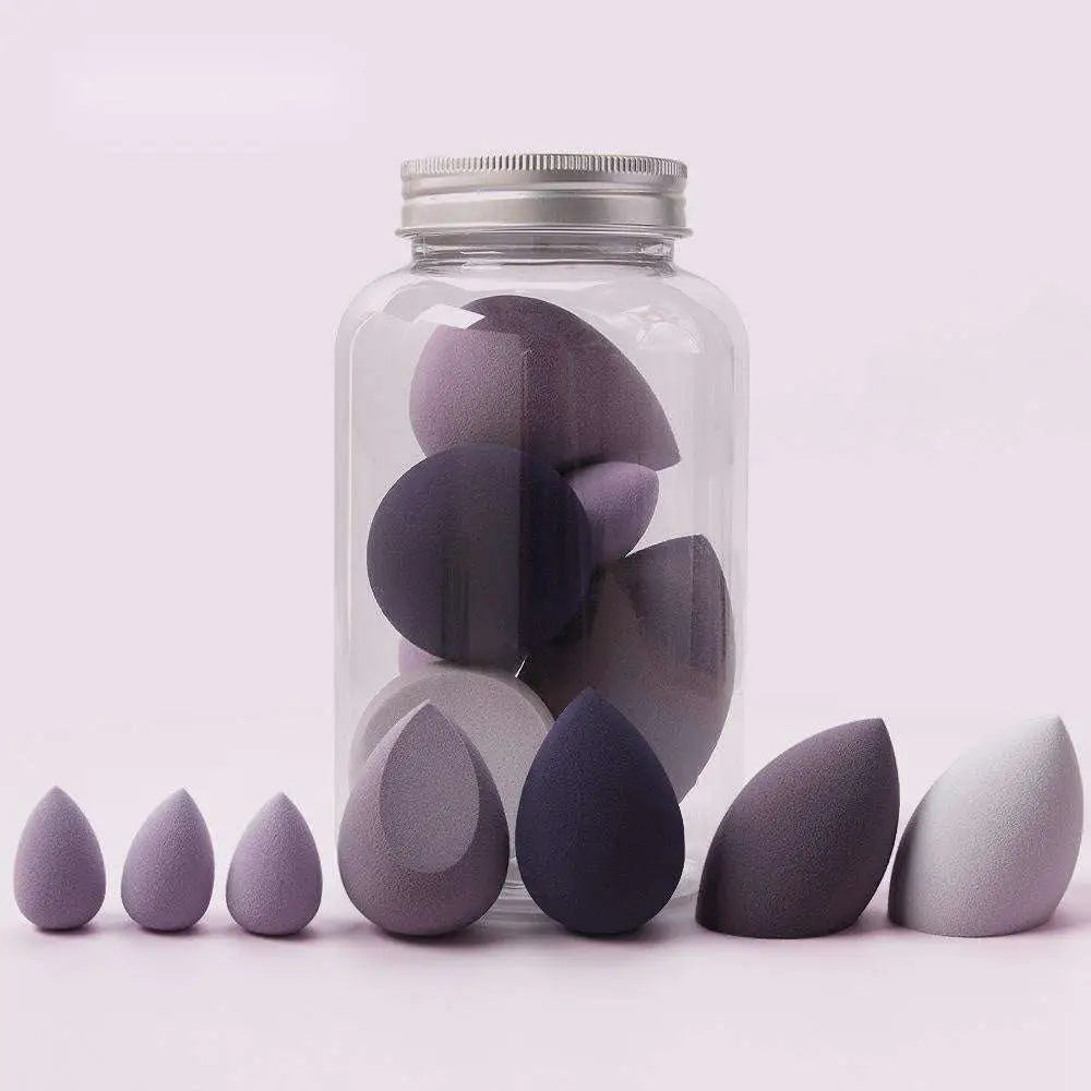 A set of multicolored spherical beauty egg makeup sponges in gray and purple made of hydrophilic polyurethane surrounding a jar