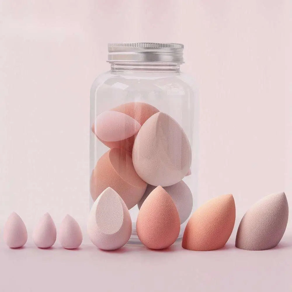 A collection of pastel pink and peach hydrophilic polyurethane egg makeup sponges arranged around a clear jar with silver lid