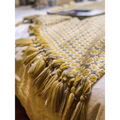 A cozy mustard yellow and cream knitted sofa blanket with geometric pattern and braided tassels along the edge