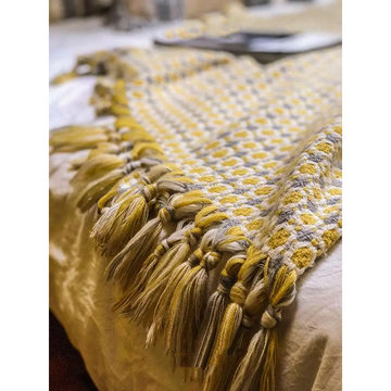 A cozy mustard yellow and cream knitted sofa blanket with geometric pattern and braided tassels along the edge
