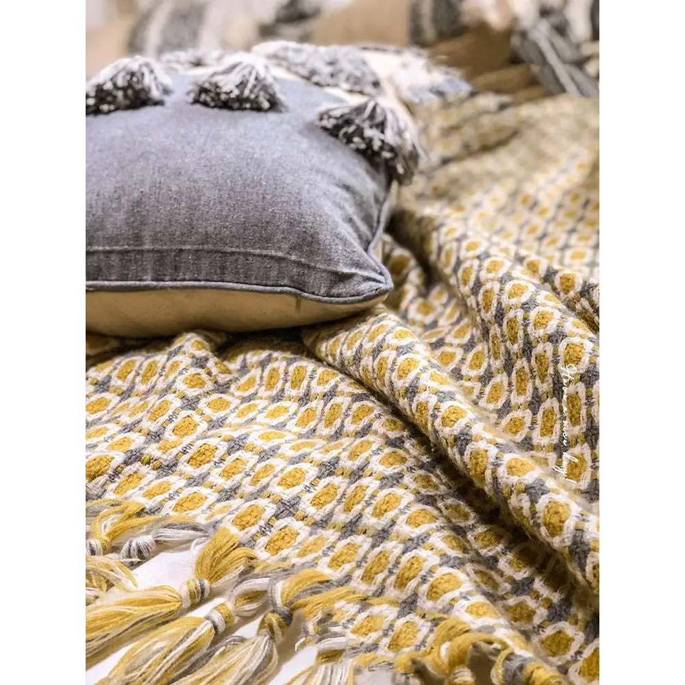 A cozy mustard yellow and cream knitted sofa blanket with geometric pattern and braided tassels along the edge