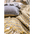 Gray denim pillow with black tassels resting on mustard yellow geometric knitted sofa blanket cover with tassels