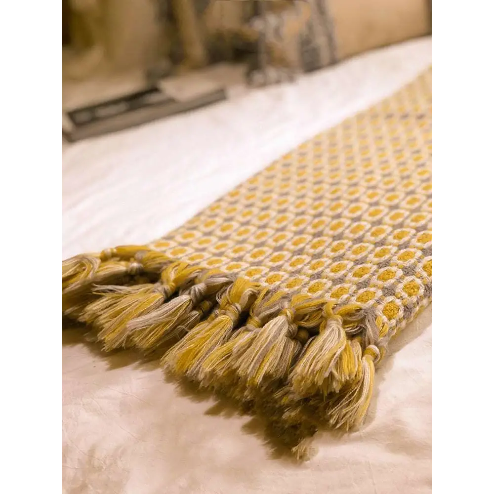 A soft mustard yellow and cream geometric knitted sofa blanket with tassels for cozy home decor