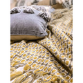Gray cushion with textured fabric and black tassels paired with mustard yellow geometric knitted sofa blanket cover