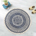 A round cream-colored carpet floor mat with intricate navy mandala ethnic style patterns and fringed edges
