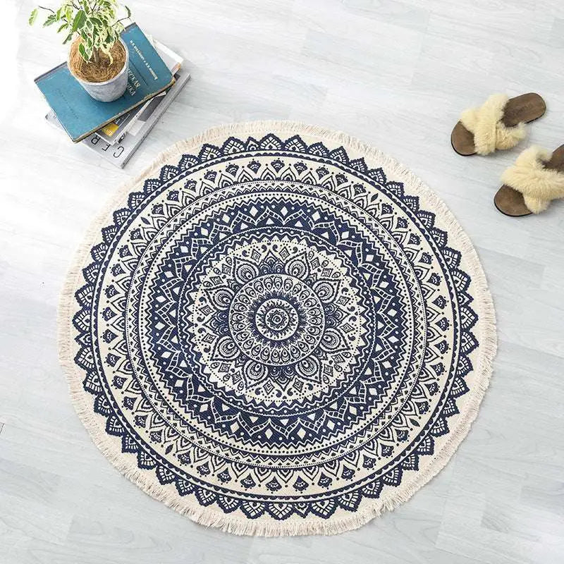 A round cream-colored carpet floor mat with intricate navy mandala ethnic style patterns and fringed edges