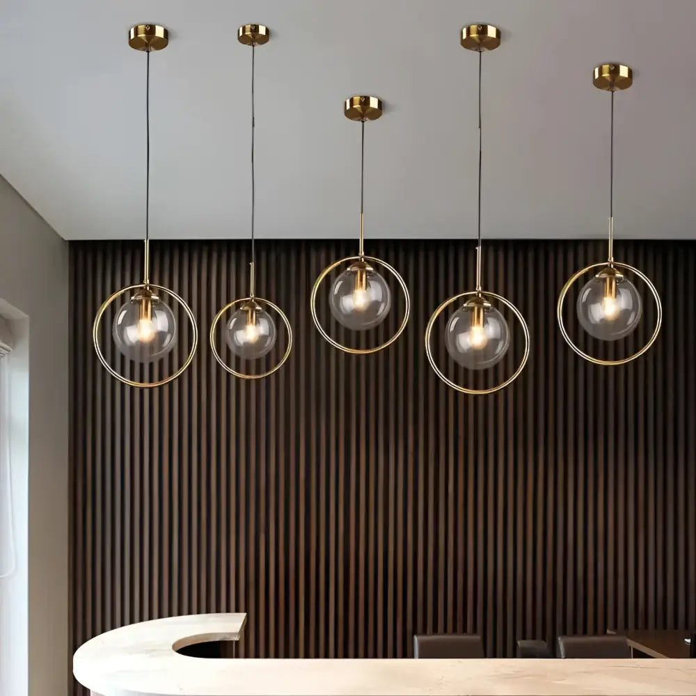 Five nordic modern minimalist glass pendant lights with gold metal frames and clear glass spheres hanging from ceiling