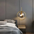 A nordic modern minimalist glass pendant light with a gold circular frame and clear globe pendant lamp above bed