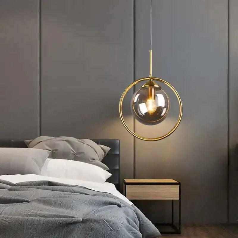 A nordic modern minimalist glass pendant light with a gold circular frame and clear globe pendant lamp above bed