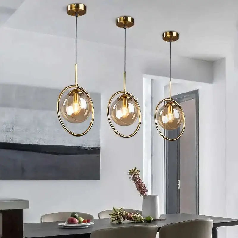 Three nordic modern minimalist glass pendant lights with gold metal frames and amber-tinted globes for indoor use