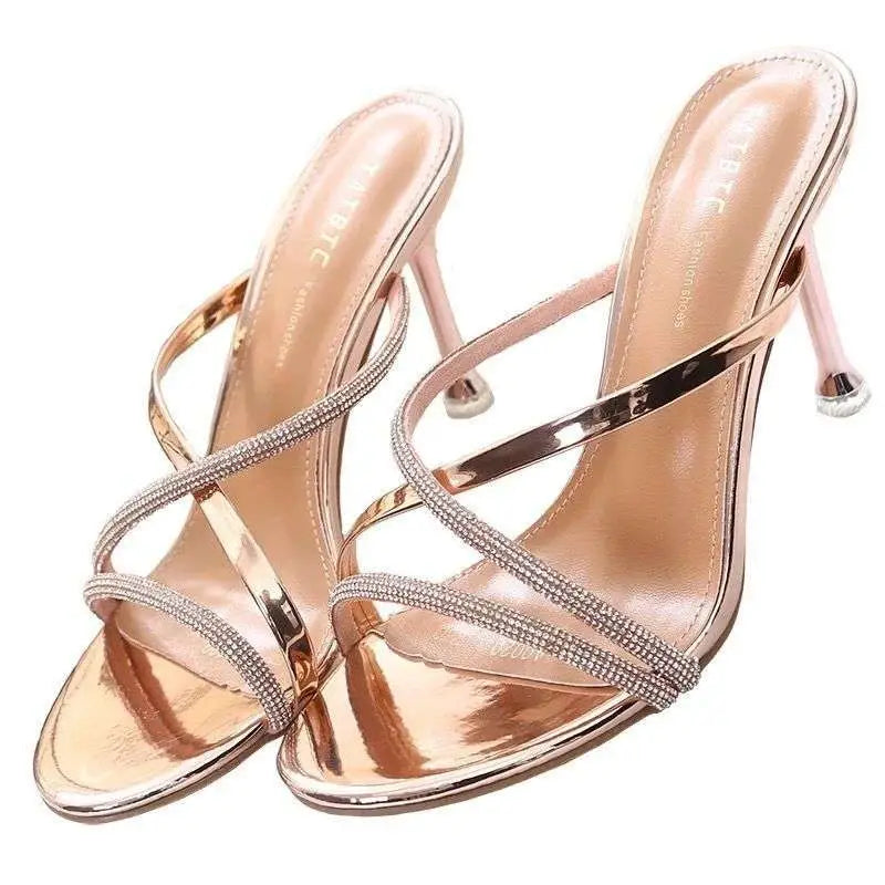A pair of nude stiletto toe high heel rhinestone sandals with slender straps and a sleek metallic heel