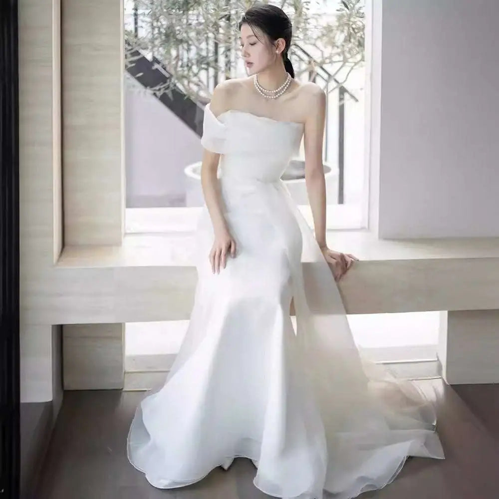 Off-shoulder satin light wedding dress with flowing white fabric, fitted bodice, and flared skirt elegant design