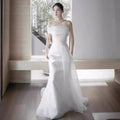 A flowing white off-shoulder satin light wedding dress with a fitted bodice and a sweeping train