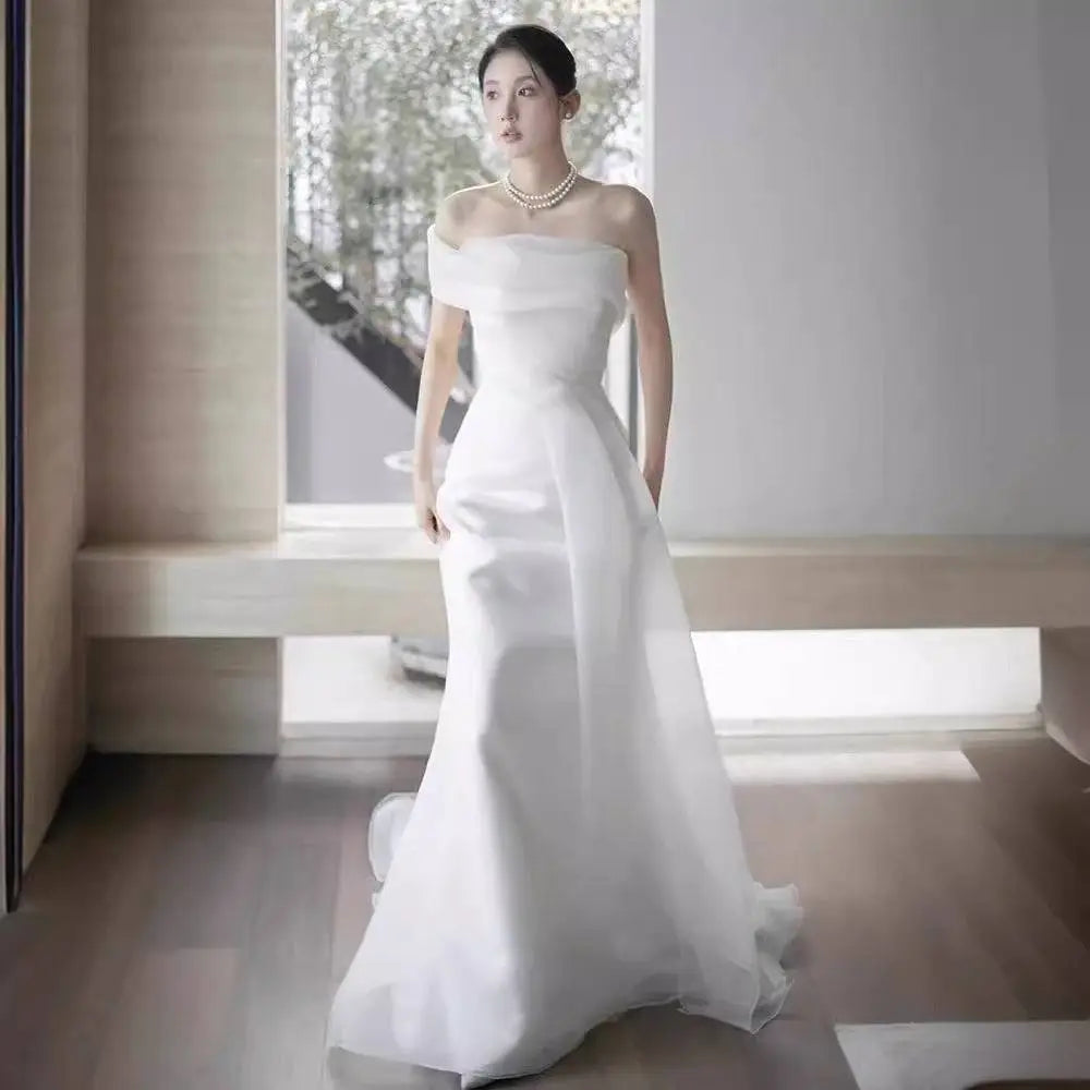 A flowing white off-shoulder satin light wedding dress with a fitted bodice and a sweeping train