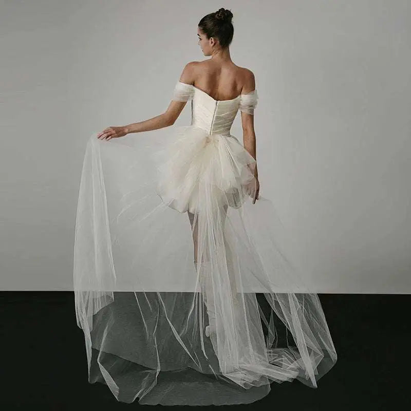 Off-shoulder tulle white wedding dress with structured bodice and layered skirt featuring a train in ivory color