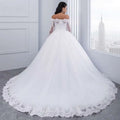 A flowing white off-the-shoulder bridal wedding lace gown with intricate detailing and a delicate tulle skirt