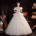A woman wearing an off the shoulder white wedding dress with lace shoulder accents and a voluminous tulle skirt