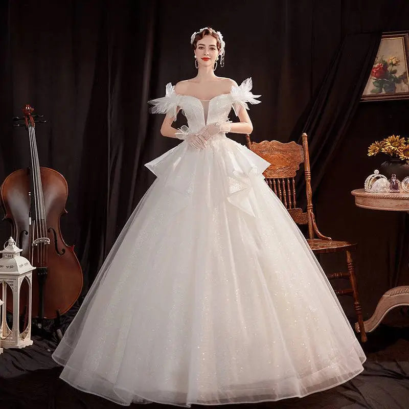 A woman wearing an off the shoulder white wedding dress with lace shoulder accents and a voluminous tulle skirt