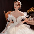 A white off the shoulder wedding dress with feathered shoulder lace tulle accents and a voluminous tulle skirt
