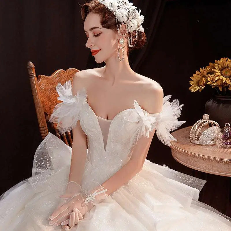 A woman wearing an off the shoulder white wedding dress with feathered shoulder lace tulle and a sparkling tulle skirt