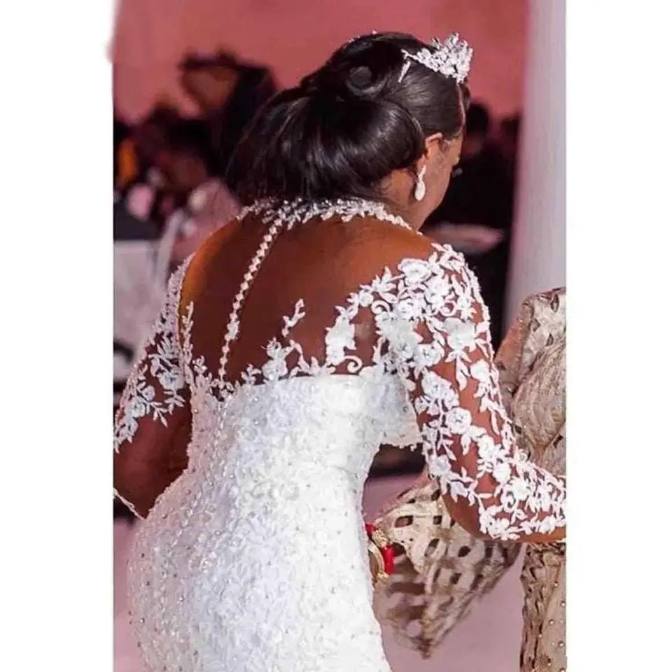 A bride wearing a long sleeves mermaid white wedding dress with off the shoulder neckline and holding a bouquet