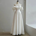 A flowing white satin light wedding dress with off the shoulder design, puffed sleeves, and delicate shoulder ties