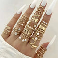 A hand wearing a gold-toned oil dripping knuckle ring set with hearts pearls butterflies and chain designs