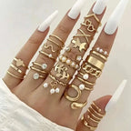 A hand wearing a gold-toned oil dripping knuckle ring set with hearts pearls butterflies and chain designs