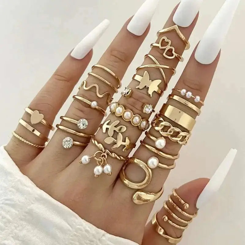 A hand wearing a gold-toned oil dripping knuckle ring set with hearts pearls butterflies and chain designs