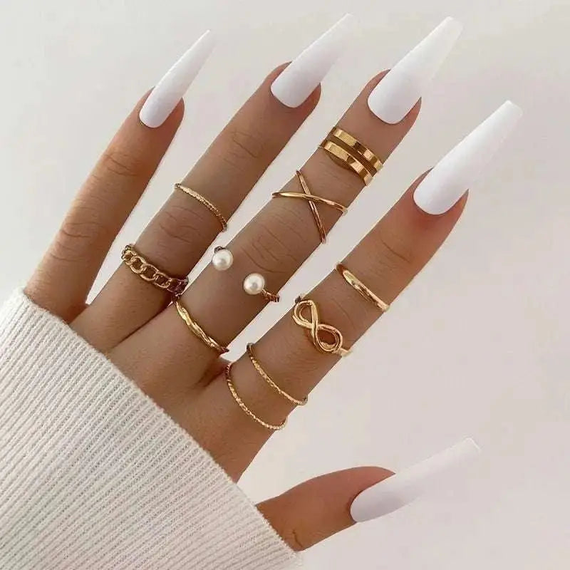 A hand wearing a gold-toned oil dripping knuckle ring set with hearts, pearls, infinity symbols, and crossed bands designs