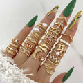 A hand wearing a gold-toned oil dripping knuckle ring set with hearts pearls eyes moons and intricate chain designs