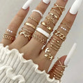 A hand wearing a gold-toned oil dripping knuckle ring set with intricate hearts, pearls, chains, and leaf designs