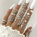 A hand wearing a silver oil dripping knuckle ring set with intricate hearts, pearls, moons, stars, and eye designs