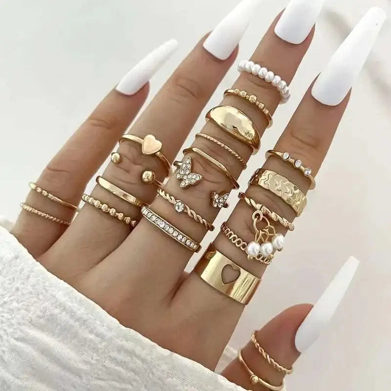A hand wearing a gold-toned oil dripping knuckle ring set featuring hearts butterflies pearls and textured designs