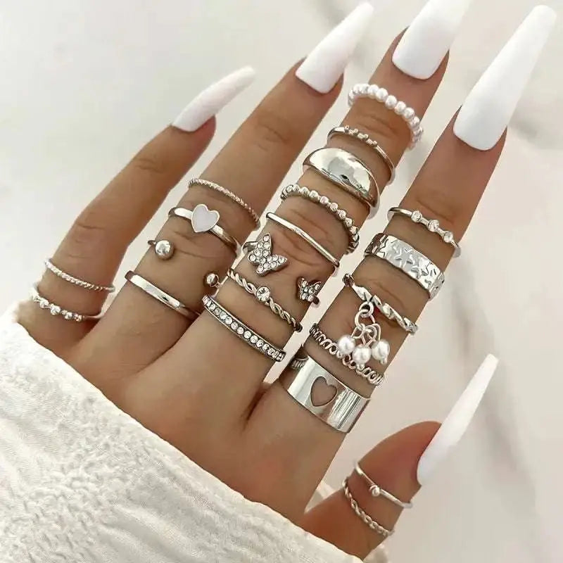 A hand adorned with a silver oil dripping knuckle ring set featuring hearts, butterflies, and pearls designs