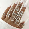 A hand wearing a silver oil dripping knuckle ring set with hearts pearls butterflies and chain designs