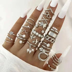 A hand wearing a silver oil dripping knuckle ring set with hearts pearls butterflies and chain designs