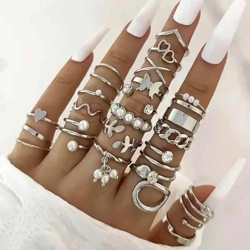 A hand wearing a silver oil dripping knuckle ring set with hearts pearls butterflies and chain designs