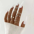 A hand wearing a silver-toned oil dripping knuckle ring set with hearts pearls and chain links designs