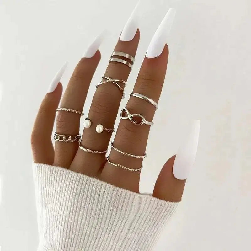 A hand wearing a silver-toned oil dripping knuckle ring set with hearts pearls and chain links designs