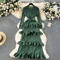 A long-sleeved olive green cake heavy industry pleated long dress with tiered ruffles and matching belt