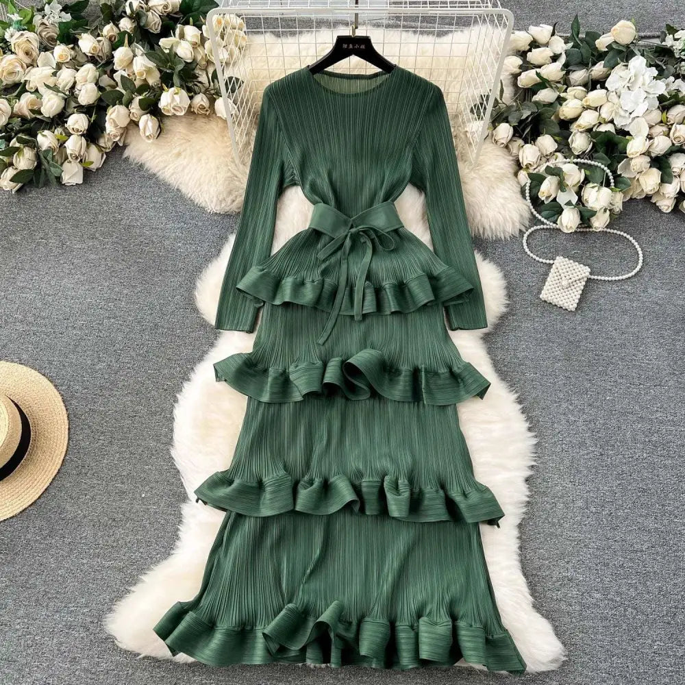 A long-sleeved olive green cake heavy industry pleated long dress with tiered ruffles and matching belt
