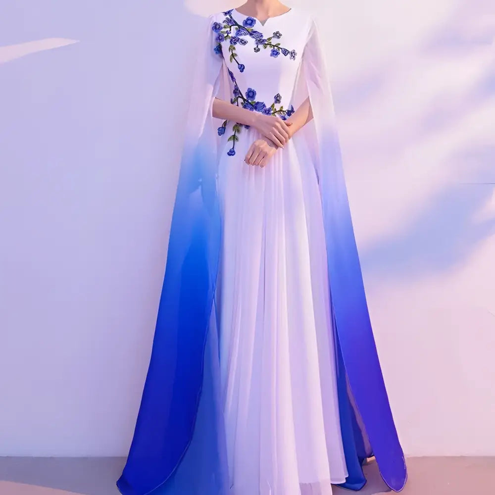 A flowing white floral choral dress with blue embroidery and an ombre cape blue for red song competition events