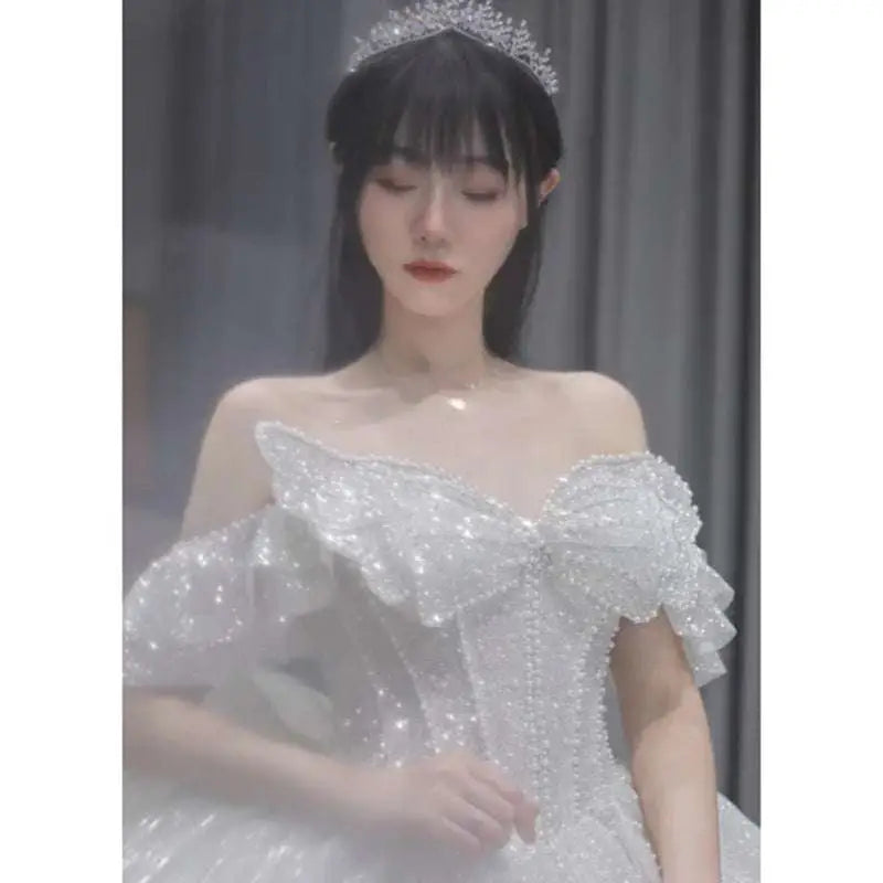 A sparkling white one-shoulder wedding dress with intricate beading and a voluminous bow in a long trailing heavy industry style