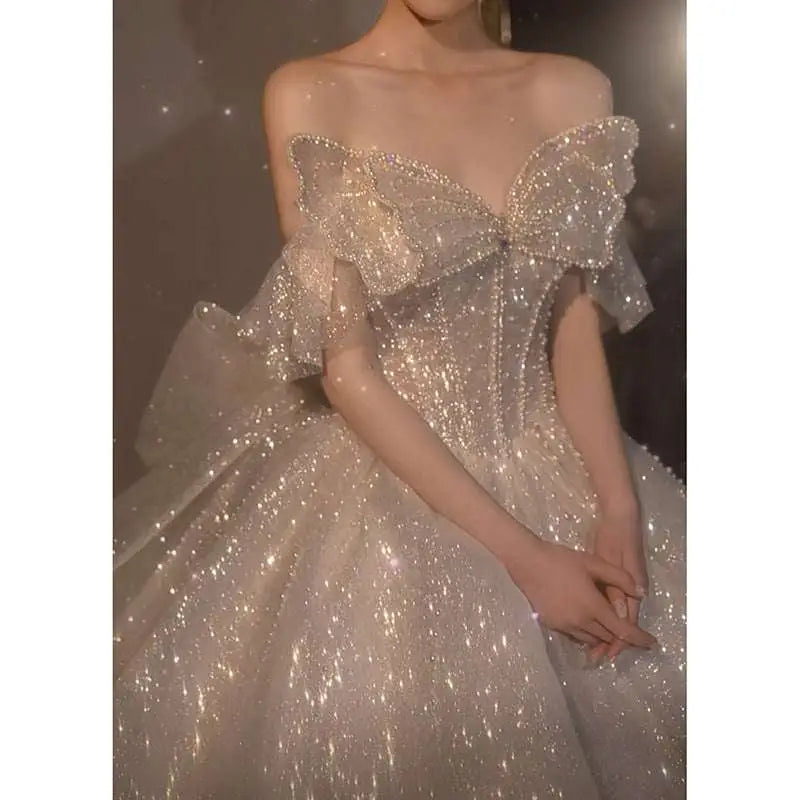 A shimmering off-the-shoulder one-shoulder wedding dress with a large sparkling bow and delicate beading, long trailing heavy industry wedding dress