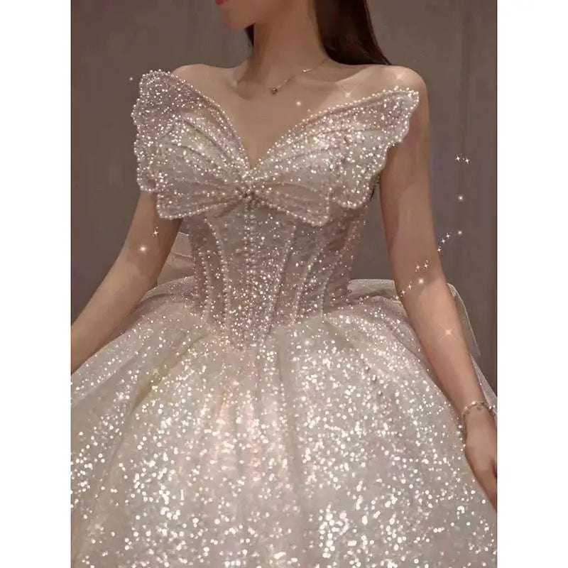 A shimmering off-white one-shoulder wedding dress with intricate beading, sequins, and a dramatic neckline bow