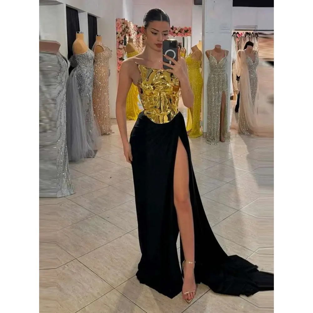 A one-shoulder slit mop black dress two-piece set with a metallic gold bodice and flowing black skirt featuring a high slit