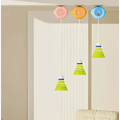 Three colorful indoor badminton trainer shuttlecocks with pastel caps and green feathers hang from orange ceiling holders for hand-eye coordination and racket control