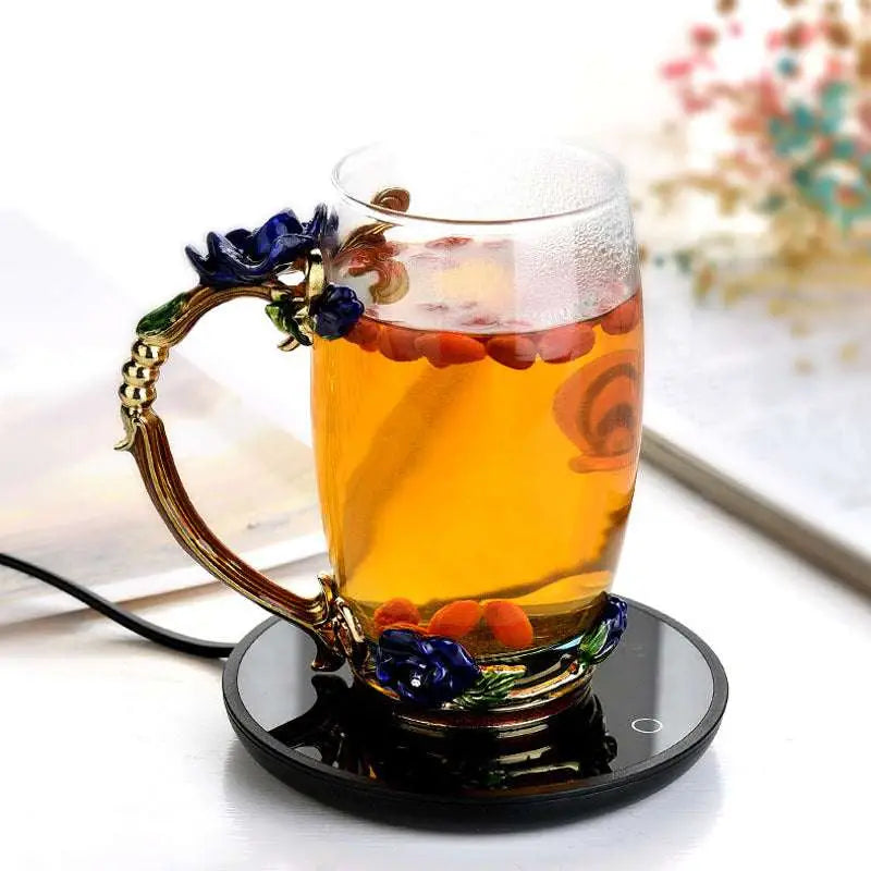 Ornate glass mug cup warmer with gold-toned handle and blue floral design filled with amber tea and goji berries